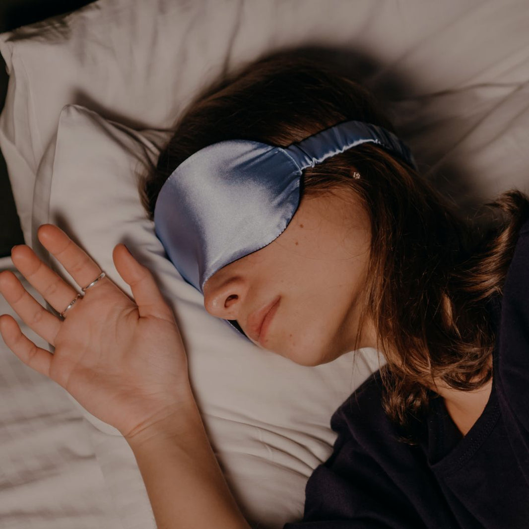 Person wearing a blue satin sleep mask lying on a pillow.