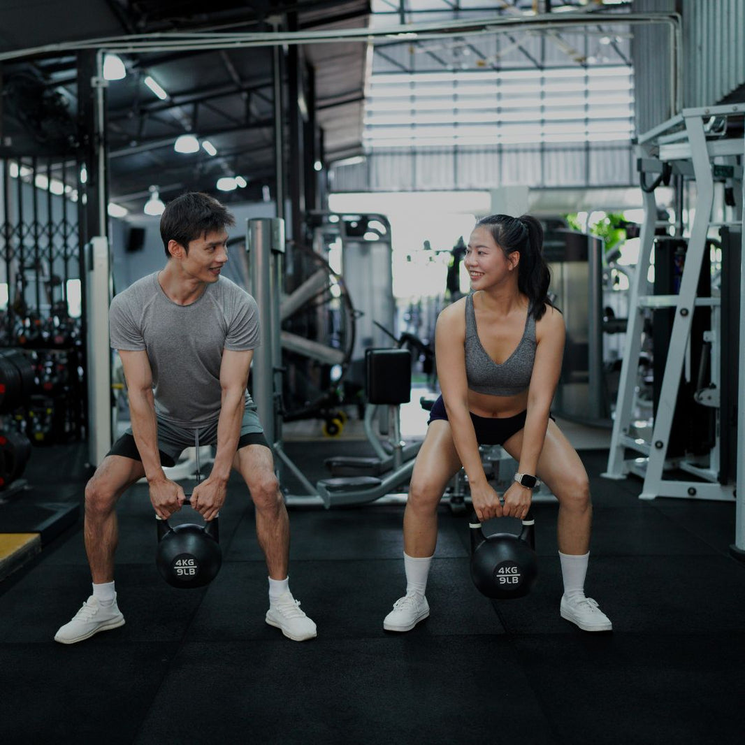 Two people exercising with kettlebells in a gym setting