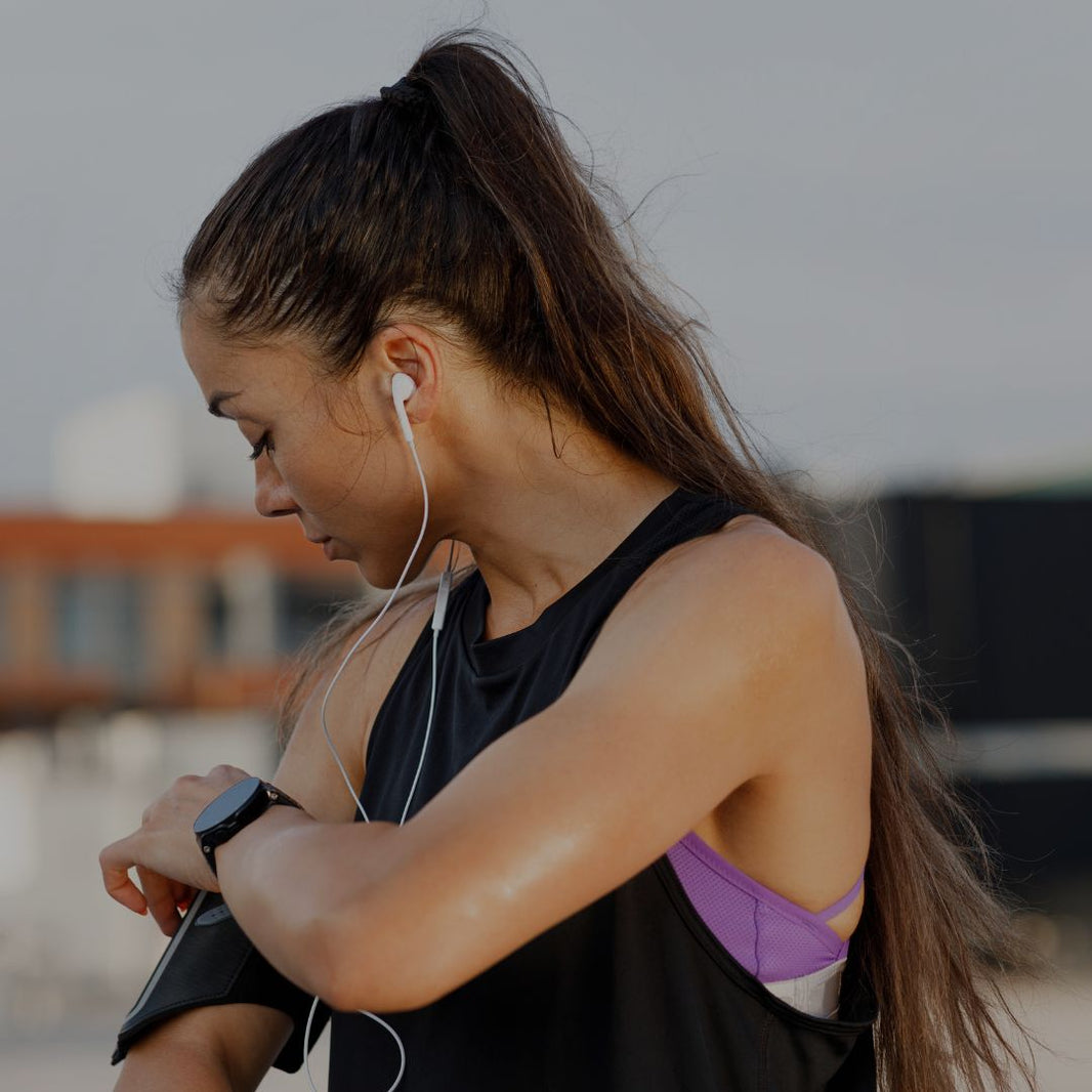 Woman exercising outdoors, looking at her watch with earphones in.